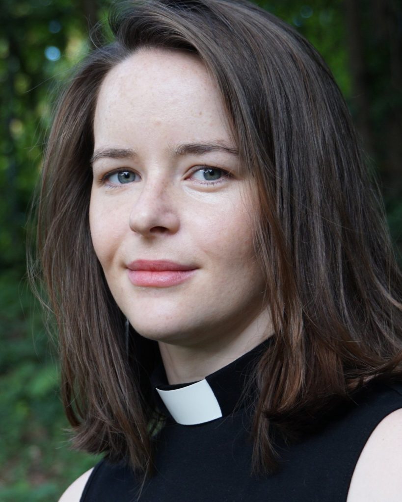 A young white woman with shoulder length brown hair wearing a priest's collar
